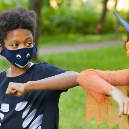 Two kids touch elbows as a greeting. They are wearing masks covering their mouths