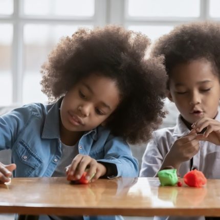 Little african american girl and boy kids have fun play with plasticine or modeling clay at home together, small children siblings engaged in creative activity with colorful playdough, hobby concept